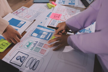 Close up ux developer and ui designer brainstorming about mobile app interface wireframe design on table with customer breif and color code at modern office.Creative digital development agency.