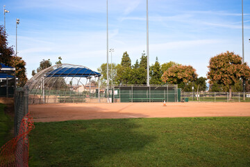 Empty baseball field with dirt infield and backstop at a public sports park in Corona, California under clear skies.