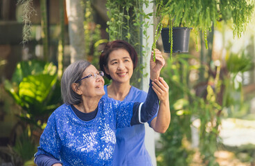 Happy senior woman enjoying gardening therapy with caregiver in nursing home backyard.