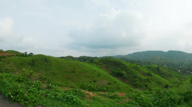 4K shot of green grass on Rayta hills and dark clouds in sky as seen from moving vehicle. Green forest in Sahyadri range at Udaipur, Rajasthan, India. Nature, environment and ecosystem concept.