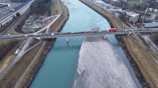 Aerial drone flight crossing the bridge over the Rhine between Liechtenstein and Switzerland, capturing cars in traffic as they leave Liechtenstein toward Switzerland, highlighting river, bridge, and 