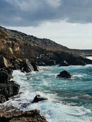 Rugged cliffs rise above the restless, foaming waves of the Mediterranean at Cape Greco Peninsula, Cyprus, creating a dramatic coastal landscape bathed in natural light