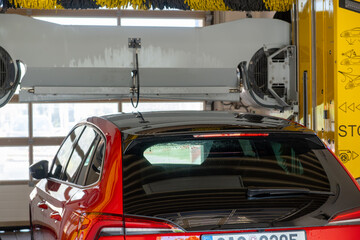 Fototapeta premium Red car passing through an automatic car wash, water and brushes cleaning the vehicle.
