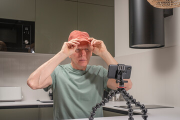 Man preparing to record a vlog at home while adjusting a cap in front of a smartphone mounted on a