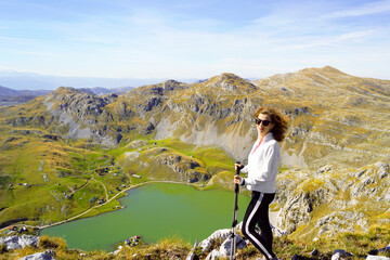 Naklejka premium Woman with trekking poles near Kapetanovo Lake in Moraca mountains. Symbolizes wellness through movement, solo adventure travel, balance between effort and calm environment, and nature focused tourism