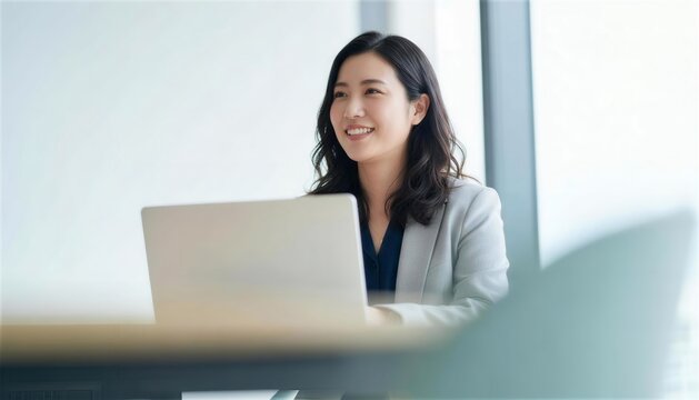 明るいオフィスで微笑みながらパソコン作業をする女性