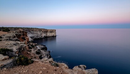 Dramatic coastal cliffs meet the serene ocean waters under a tranquil twilight sky, showcasing the peaceful beauty of a vast natural landscape at dawn or dusk
