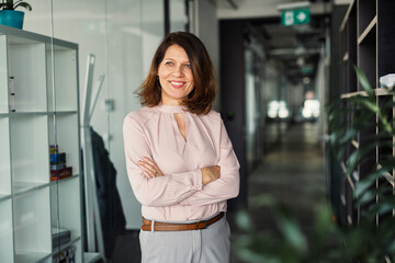 A portrait of businesswoman resting in an office, scrolling on smartphone.