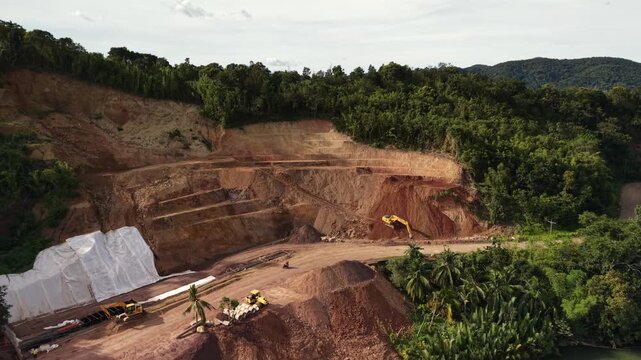 Active hillside quarry in Busuanga Palawan with excavators terraced red earth walls and tropical forest surrounding the worksite