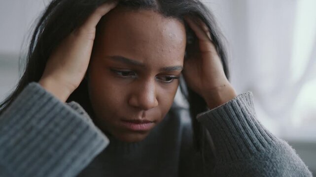 Vertical portrait of young african woman feeling headache, exhausted freelancer at home office, worker or student sitting at table with laptop in kitchen and holding head, tiredness by online job