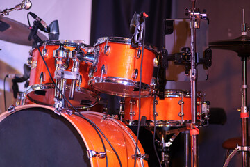Close-up of orange drum kit on stage. Detailed close-up of an orange drum kit on a live stage, cymbals, microphones, and stands ready for a music performance.