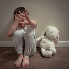 A frightened child sits on the floor covering their face, symbolizing fear, trauma, and emotional impact of domestic abuse at home.