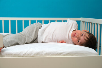 Small boy lying on his back in a white crib, looking directly at the camera with innocent eyes. Childhood portrait for baby care and parenting concepts. Child aged 4 years (four years old)