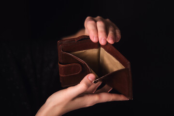 Woman hands holding an empty wallet with no money on a dark background. Financial crisis concept, poverty, and bankruptcy for economic.
