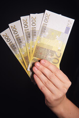 Woman holding several 200 euro banknotes in her hand, on a black background, representing financial success and wealth.