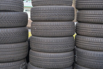 Obraz premium Tall stacks of used black rubber car tires arranged outdoors, repeating circular patterns and textured tread surfaces visible.