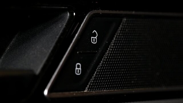 Close up view of human finger pressing unlock button on car door control panel, illuminating button symbol. Action signifies security release, preparing vehicle for occupant entry or exit