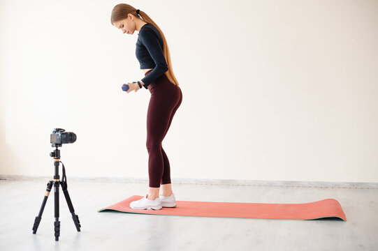 Woman filming her home workout with dumbbells and a camera on a tripod