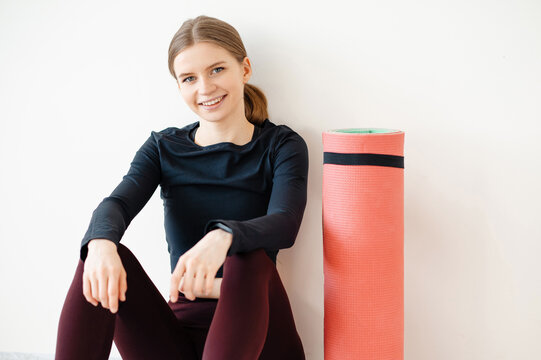 Young woman in athletic wear smiling and sitting next to a rolle