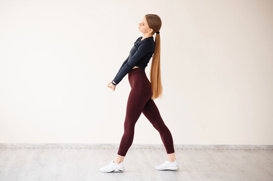 Young woman with long blonde hair in athletic wear stretching indoors