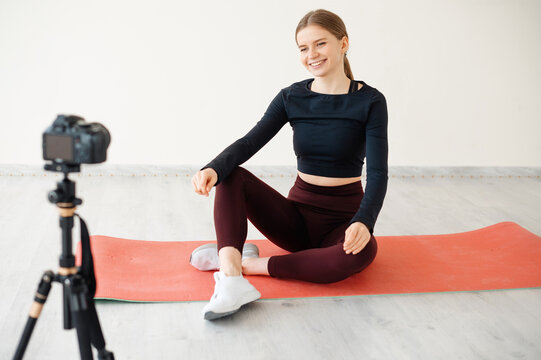 Girl recording fitness video blog on camera while sitting on yoga mat