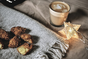 Cozy coffee cup with latte art next to warm cookies on textured blanket and decorative star light adding soft mood