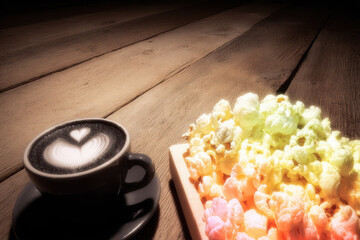 Black coffee cup with heart latte art and colorful popcorn on wooden table creating cozy warm mood
