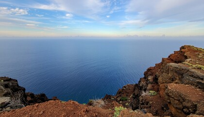 A breathtaking view from the cliff edge overlooking the vast, deep blue ocean under a partly cloudy sky