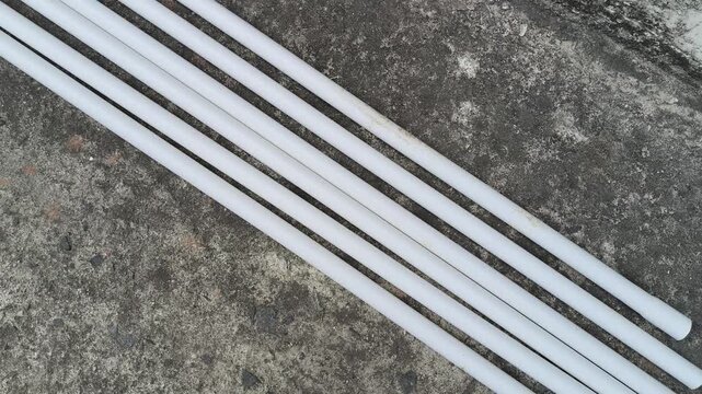 Electrical PVC pipes. White, rigid plastic pipes are laid on an old, gray concrete surface next to a textured wall. These pipes are used for electrical wiring.