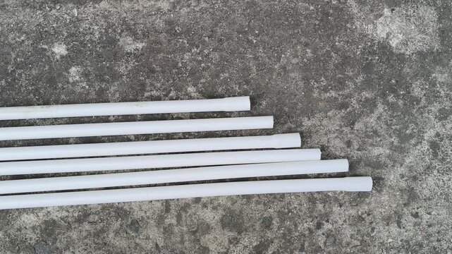 Electrical PVC pipes. White, rigid plastic pipes are laid on an old, gray concrete surface next to a textured wall. These pipes are used for electrical wiring.