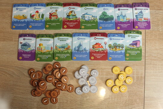 Mozyr, Belarus, April 10 2024: preparation for the board game Machi Koro. Laid out upgrade cards and coins on the table. Upper angle. Home Entertainment