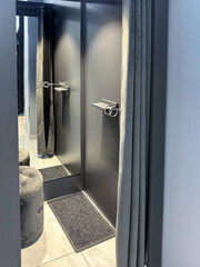 Modern fitting room with mirror, gray curtain, and stool.