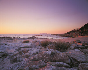 Peaceful rocky shoreline at sunset with soft pastel sky gentle waves and warm evening light creating a serene coastal landscape