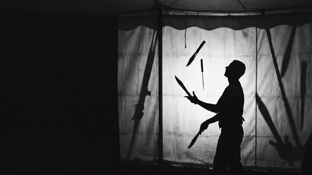 Man performing dangerous knife juggling circus act. Silhouette of juggler with knives on a white curtain. Entertainment show at chapiteau.