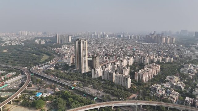 Cinematic aerial shot of Noida showing a linear expressway framed by trees and city structures.