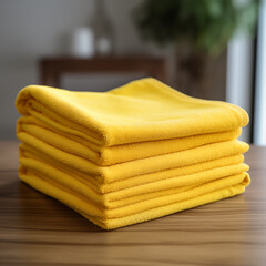 Zestaw puszystych, ż&oacute;łtych ręcznik&oacute;w złożonych w kostkę na drewnianym blacie. Estetyczne i miękkie tekstylia domowe.