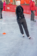 Obraz premium Rear view of woman on ice in black jacket. Woman skating on outdoor ice rink in winter clothes. Concept of sport, winter fun and seasonal recreation
