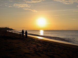 Silhouette of family enjoying a sunset walk on the beach with golden light reflecting on the water for a tranquil vacation moment