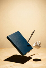 Minimalist levitating stationery set with blue notebook, pen, and coffee cup on wooden desk.