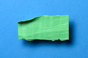 One single green torn ripped wrinkled crumpled blank paper note with drop shadow, folded edge and copy space for text on blue background
