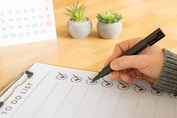 Hand ticking circles on a to do list document attached to a clipboard, representing successful completion of tasks during focused planning and organization