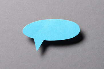 Blue blank cut out paper speech bubble with shadow and copy space for text on gray background, close-up flat lay top view conceptual backdrop