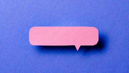 Pink blank cut out paper speech bubble with shadow and copy space for text on blue background, close-up flat lay top view conceptual backdrop