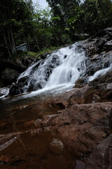 Fototapeta premium beautiful waterfall with trees and coral. water flows over dark, rugged stones, rocks creating staircase effect. The scene is serene natural landscape.