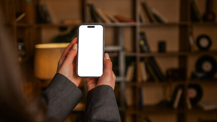 Person holding a smartphone with a blank white screen in front of a bookshelf