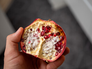 Half pomegranate fruit held in hand, fresh red seeds and natural texture, close up food detail.