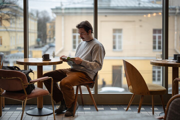 Handsome focused man book lover enjoying reading book in cozy coffee shop on work break. Smart male...