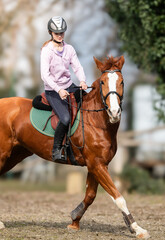 A young girl riding a chestnut horse in rural countryside.