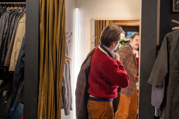 Male customer in men's wear second hand boutique trying on vintage fashionable checkered blazer in...