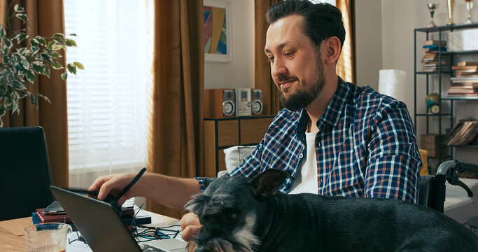 A smiling man in a white blouse and plaid shirt talks to his colleague about a new bank client impressed by the offer, while filling out final documents next to his open laptop.